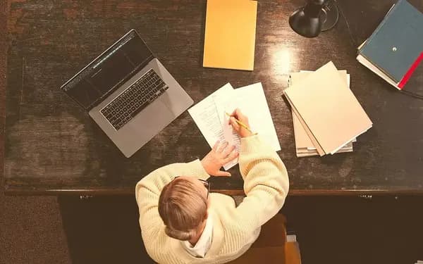 An author marking up pages at a desk beside an open laptop