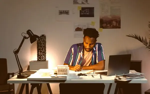 A writer working late at a desk lamp, beside a laptop and printed pages