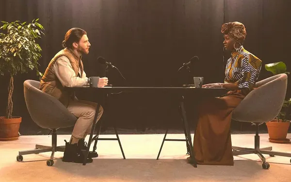 Two podcasters talking across a table with studio microphones