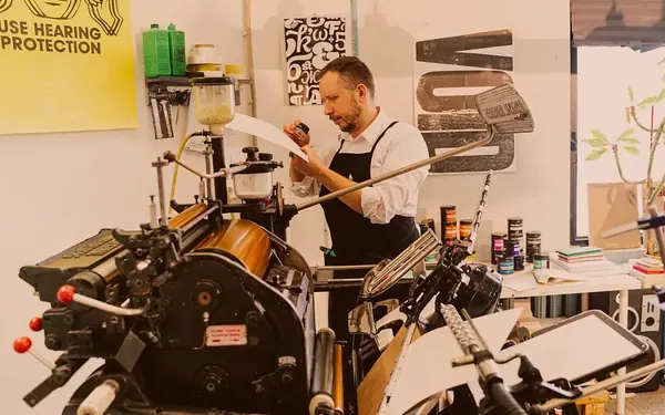 A printer checking a freshly pulled proof sheet beside a letterpress